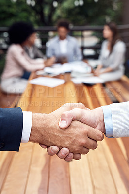 Buy stock photo Cropped shot of two unrecognizable businessmen shaking hands while their colleagues sit behind them outdoors