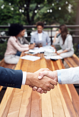 Buy stock photo Cropped shot of two unrecognizable businessmen shaking hands while their colleagues sit behind them outdoors