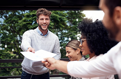 Buy stock photo Cropped shot of a handsome young businessman standing and passing out documents to his seated colleagues during an outdoor meeting