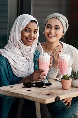 Buy stock photo Cropped portrait of two affectionate young girlfriends having milkshakes together at a cafe while dressed in hijab