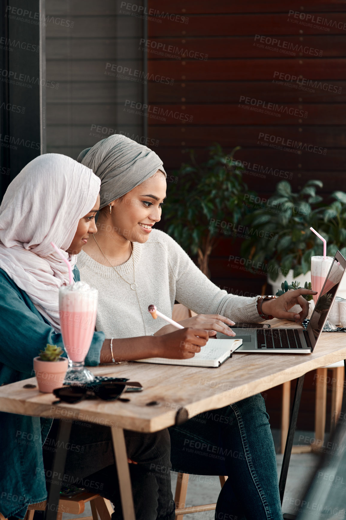 Buy stock photo Cropped shot of two affectionate young friends using a laptop together at a cafe while dressed in hijab