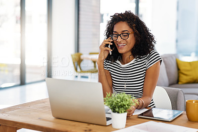 Buy stock photo Cropped shot of an attractive young businesswoman sitting in her home and talking on her cellphone while using her laptop
