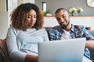 Buy stock photo Cropped shot of an affectionate young couple sitting on the sofa together and using a laptop in their living room