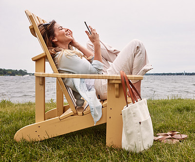 Buy stock photo Shot of an attractive young woman using a smartphone while relaxing next to the lake