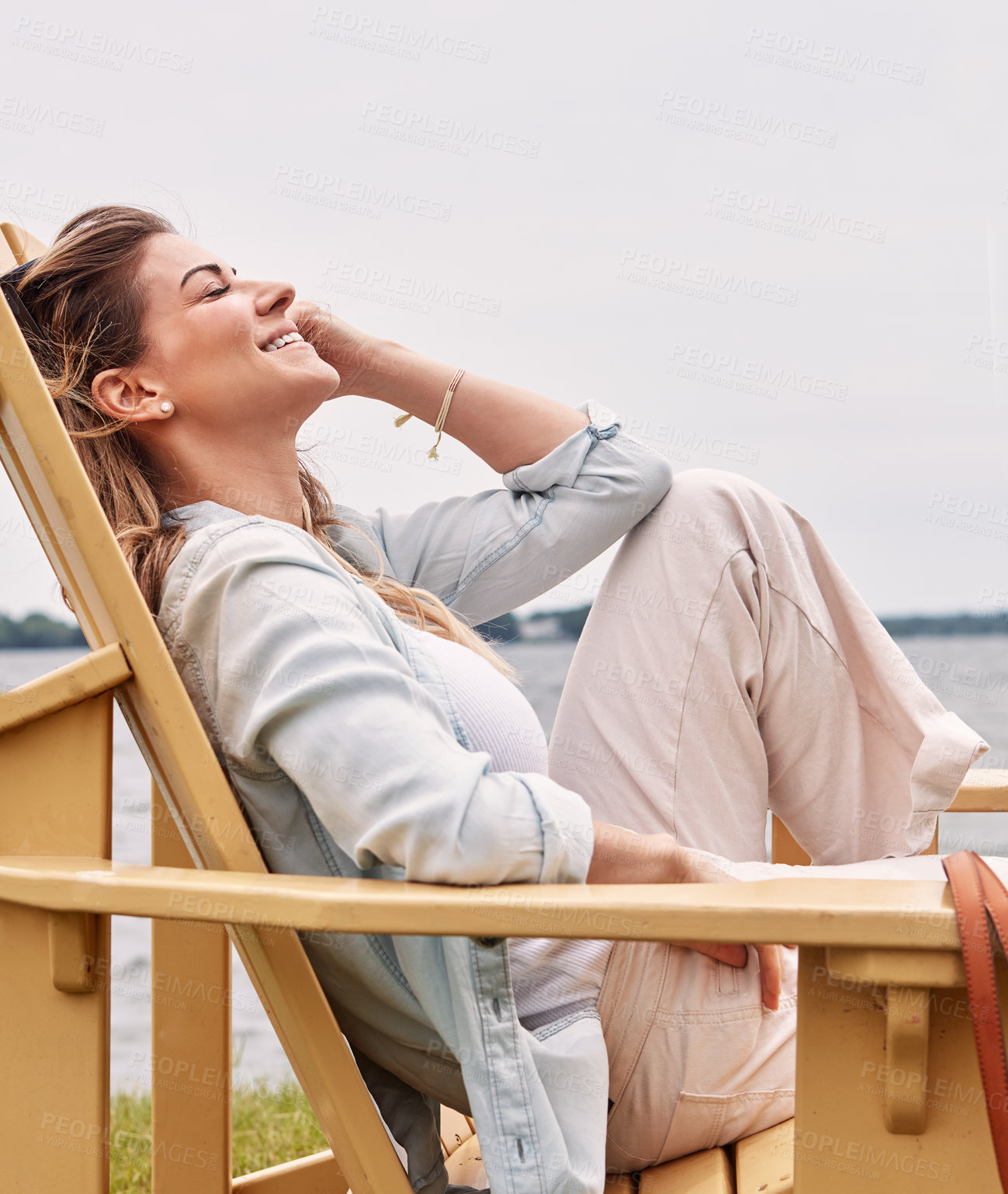 Buy stock photo Shot of a beautiful young woman relaxing on a chair next a lake