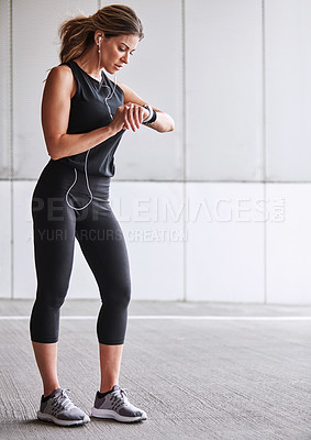 Buy stock photo Shot of a sporty young woman checking her watch while exercising outdoors