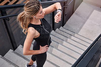 Buy stock photo High angle shot of a sporty young woman checking her watch while exercising outdoors
