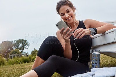 Buy stock photo Shot of a sporty young woman using a cellphone while exercising outdoors