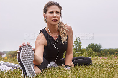 Buy stock photo Shot of a sporty young woman stretching her legs while exercising outdoors