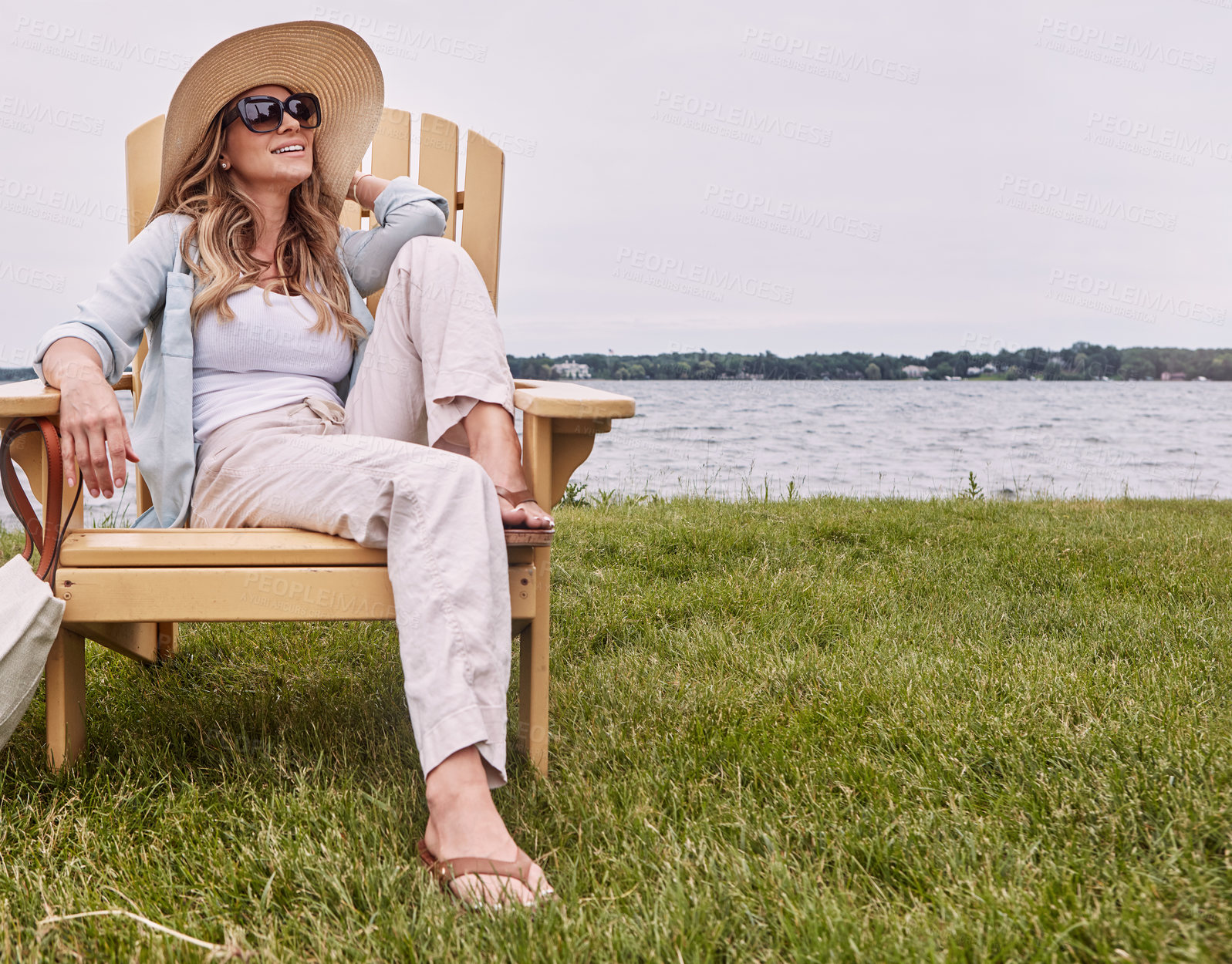 Buy stock photo Shot of a beautiful young woman relaxing on a chair next a lake