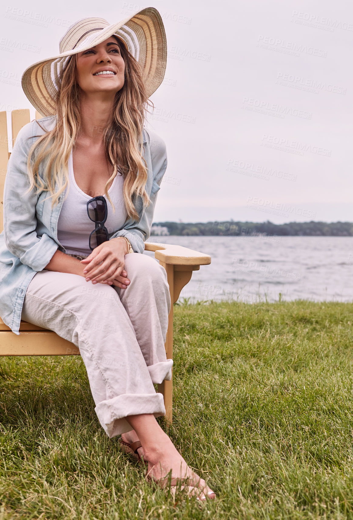 Buy stock photo Shot of a beautiful young woman relaxing on a chair next a lake