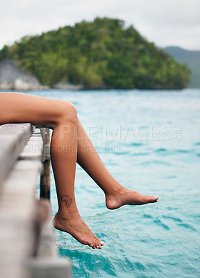 Buy stock photo Cropped shot of an unrecognizable woman sitting and dangling her legs over the edge of a boardwalk during vacation