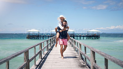 Buy stock photo Ocean, dock and a couple playing on vacation for a piggy back, freedom and to relax outdoor with love. A man and woman together on holiday, tropical travel and summer adventure in nature with water