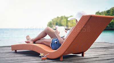 Buy stock photo Full length shot of an attractive young woman sitting on a sun lounger and reading a book during a vacation