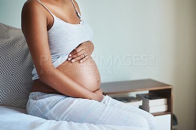 Buy stock photo Shot of an unrecognizable pregnant woman sitting on a bed and holding her belly in her bedroom at home