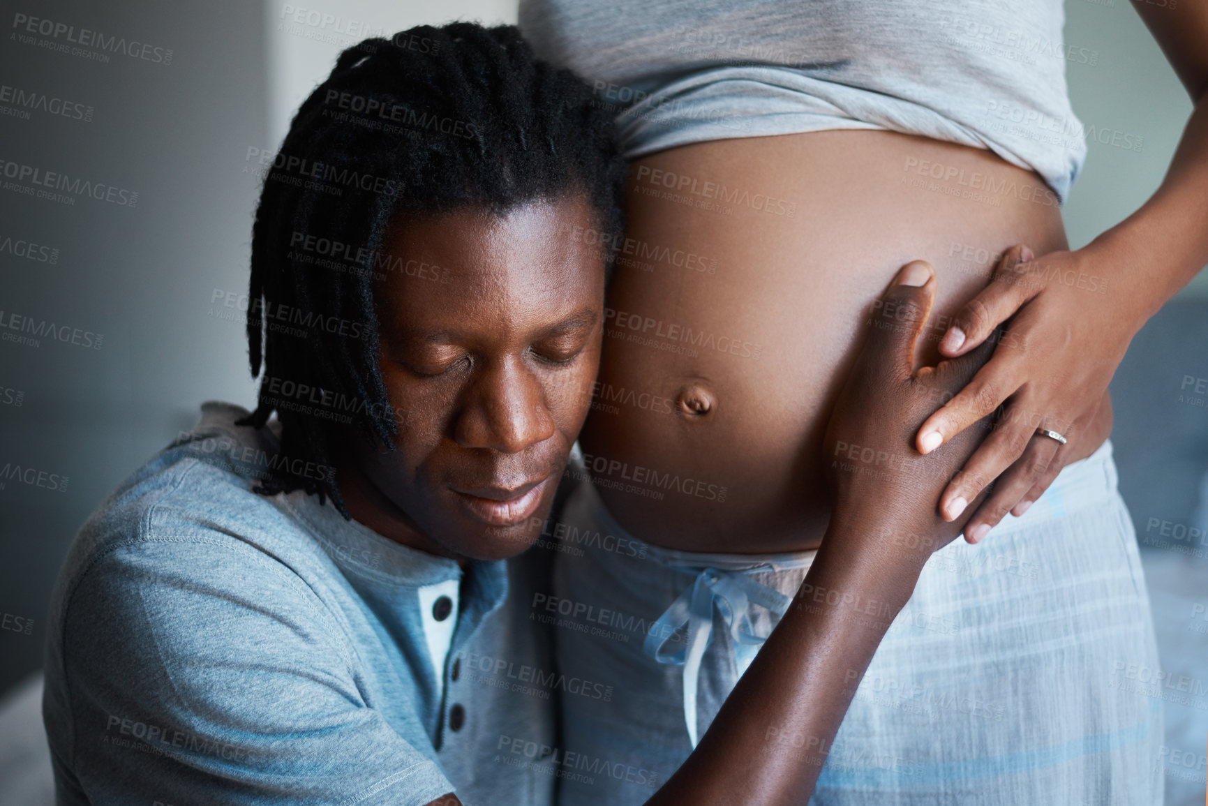 Buy stock photo Cropped shot of a happy young man holding and listening to his pregnant wife's belly at home