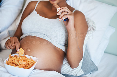 Buy stock photo Cropped shot of unrecognizable pregnant woman eating potato chips and chocolate in bed