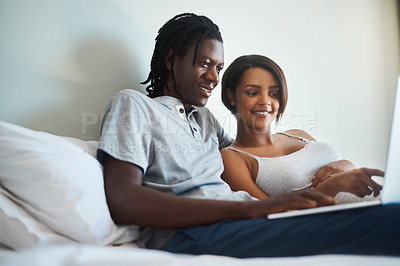 Buy stock photo Shot of an expecting young couple using a laptop together while relaxing in bed at home