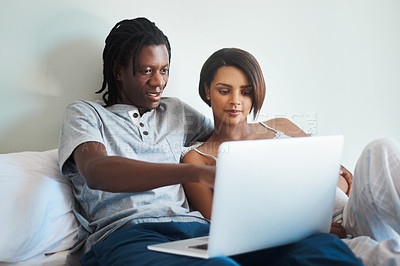 Buy stock photo Shot of an expecting young couple using a laptop together while relaxing in bed at home