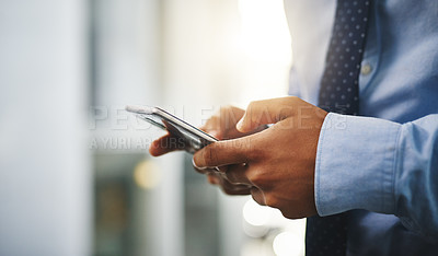 Buy stock photo Cropped shot of an unrecognizable businessman standing alone in the office and using his cellphone to text