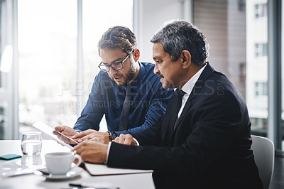 Buy stock photo Cropped shot of two businessmen sitting together and working on a tablet in the office
