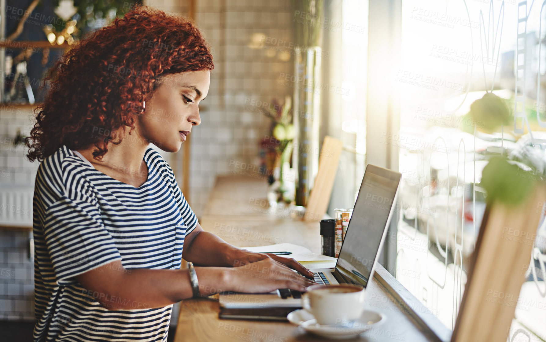 Buy stock photo Cropped shot of an attractive young businesswoman sitting alone and blogging from her laptop while inside a cafe