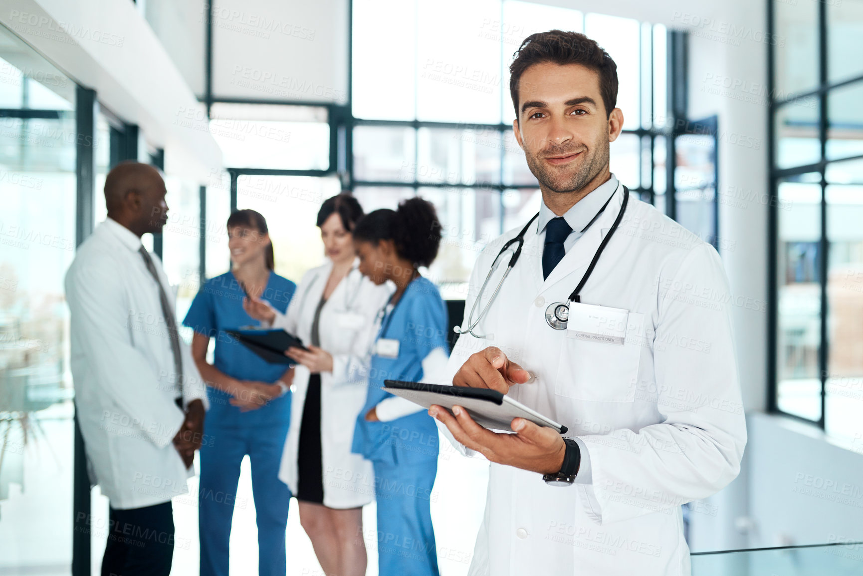 Buy stock photo Portrait of a young doctor using a digital tablet in a hospital with his colleagues in the background