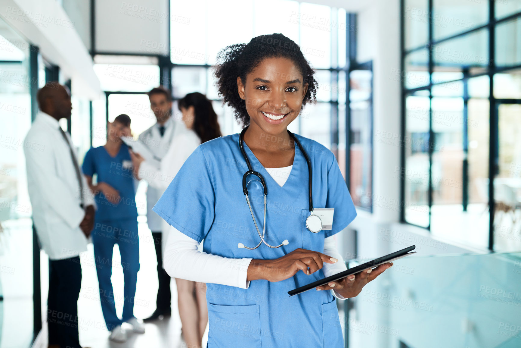 Buy stock photo Portrait of a young doctor using a digital tablet in a hospital with her colleagues in the background