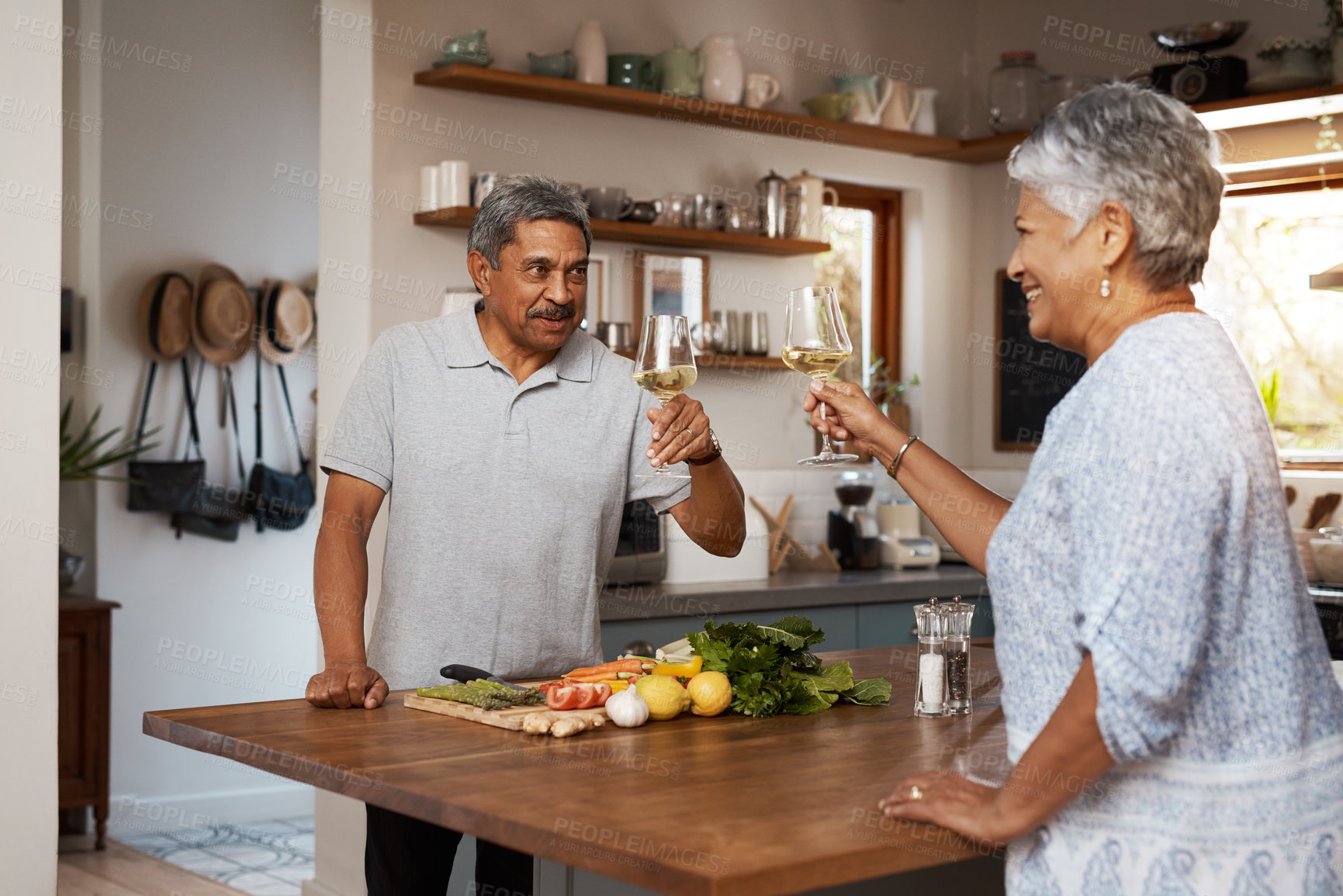 Buy stock photo Shot of a happy mature couple toasting with wine while cooking a meal together at home