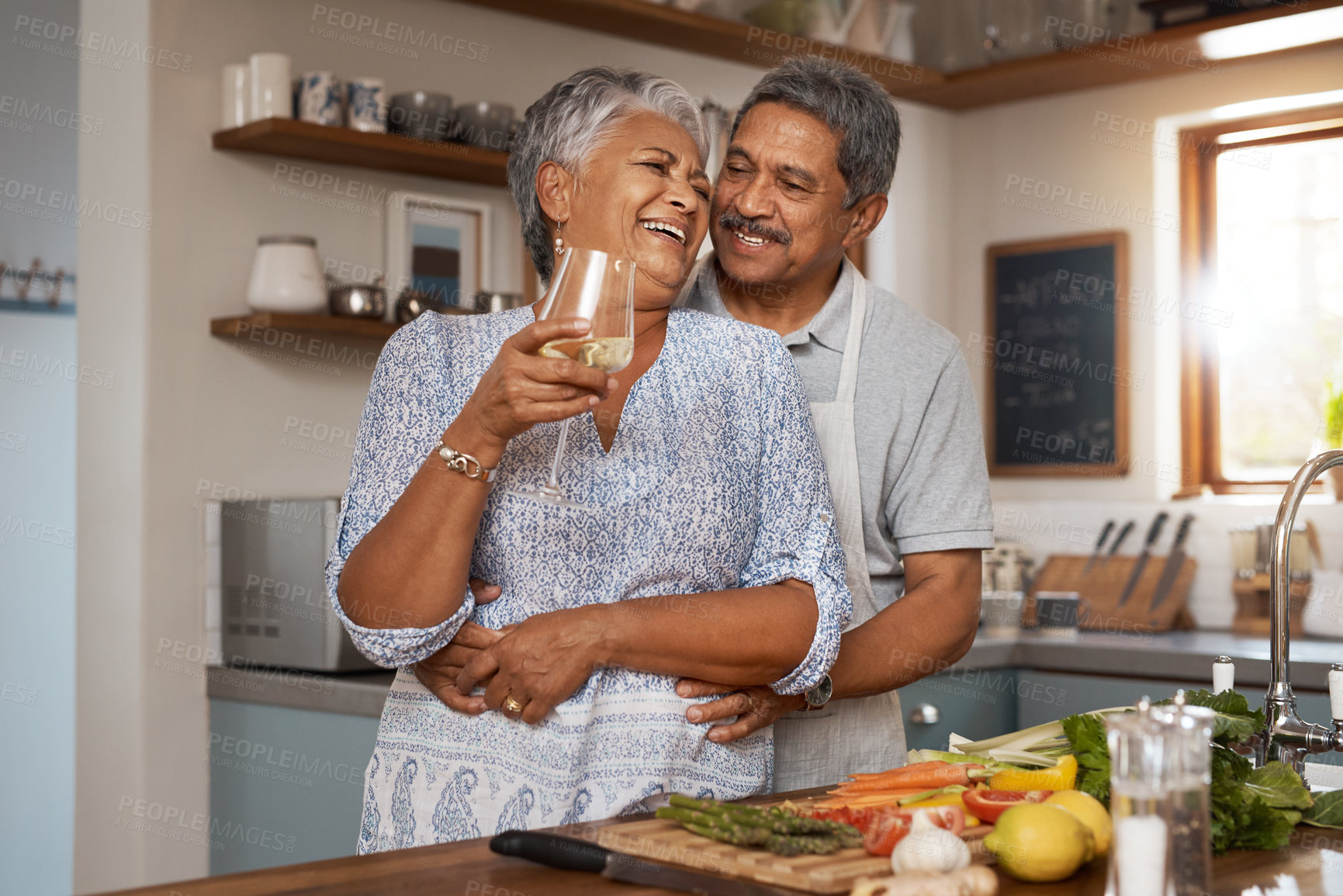 Buy stock photo Hug, old woman and man in kitchen with wine glass, happiness and cooking healthy vegetable dinner together. Smile, love and food, happy senior couple in retirement with drink, vegetables and wellness
