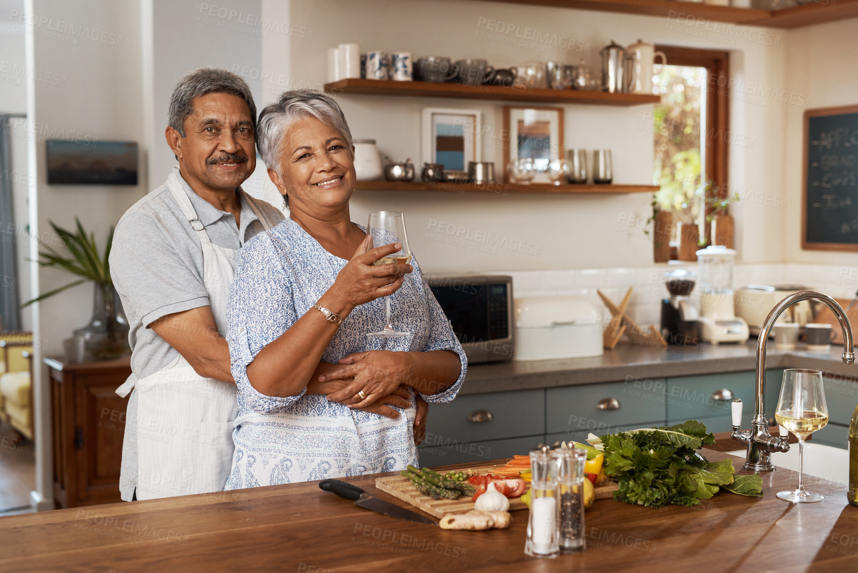 Buy stock photo Portrait of old couple at kitchen counter with wine, embrace and cooking healthy vegetable dinner together. Smile, happiness and food, senior man and happy woman with drink, vegetables and retirement