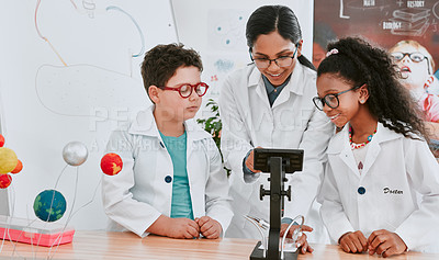 Buy stock photo Shot of a young science teacher using a microscope with her pupils in science class at school