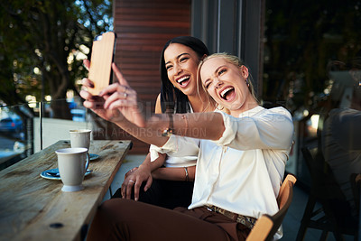 Buy stock photo Shot of two young women taking a selfie while sitting at a cafe