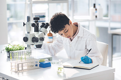 Buy stock photo Cropped shot of an attractive young female scientist making notes while working with a microscope and plants in a laboratory