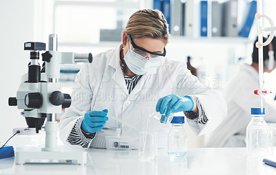 Buy stock photo Cropped shot of an attractive female scientist pouring a liquid into a beaker in a laboratory with her colleague in the background