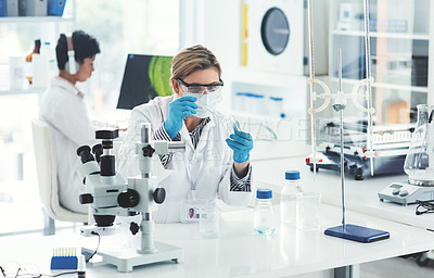 Buy stock photo Cropped shot of an attractive young female scientist dropping some liquid into a beaker in a laboratory with her colleague in the background