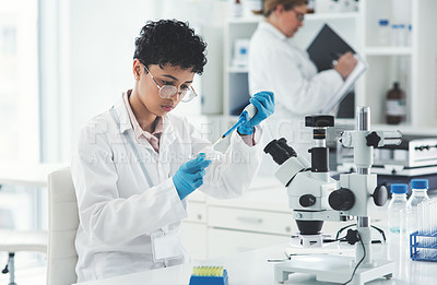 Buy stock photo Cropped shot of an attractive female scientist dropping a liquid sample into a petri dish in a laboratory with her colleague in the background