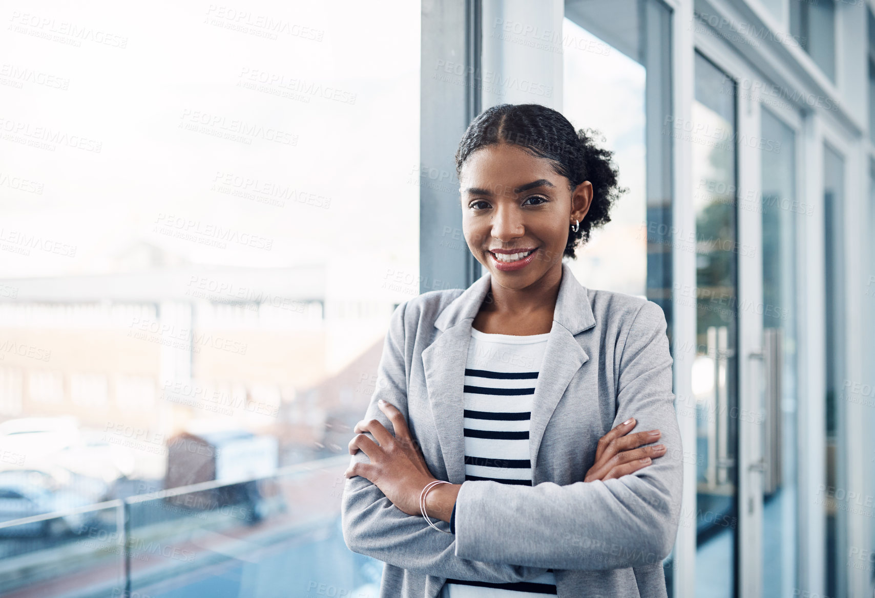 Buy stock photo Happy, confident and professional young business woman folding her arms while standing in a modern office. Portrait of a black woman leader smiling, looking proud, powerful, ready and focused 