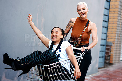 Buy stock photo Cropped shot of an energetic young woman pushing her female friend in a shopping cart outdoors