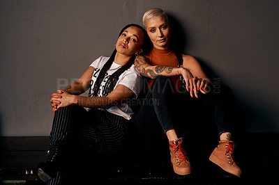 Buy stock photo Cropped portrait of two attractive young girlfriends looking serious while sitting against a dark background