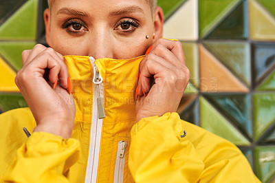 Buy stock photo Cropped portrait of an attractive young woman standing against a tiled wall and covering her mouth with her jacket