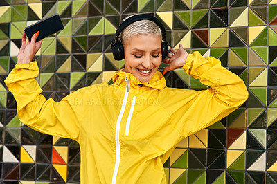 Buy stock photo Cropped shot of an attractive young woman standing against a wall and listening to music from her cellphone through headphones