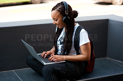 Buy stock photo Shot of an attractive young woman listening to music and using her laptop while relaxing outdoors