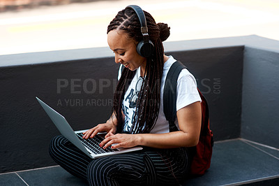 Buy stock photo Shot of an attractive young woman listening to music and using her laptop while relaxing outdoors