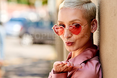 Buy stock photo Cropped portrait of an attractive young woman wearing heart shaped sunglasses and blowing a kiss while standing against a wall