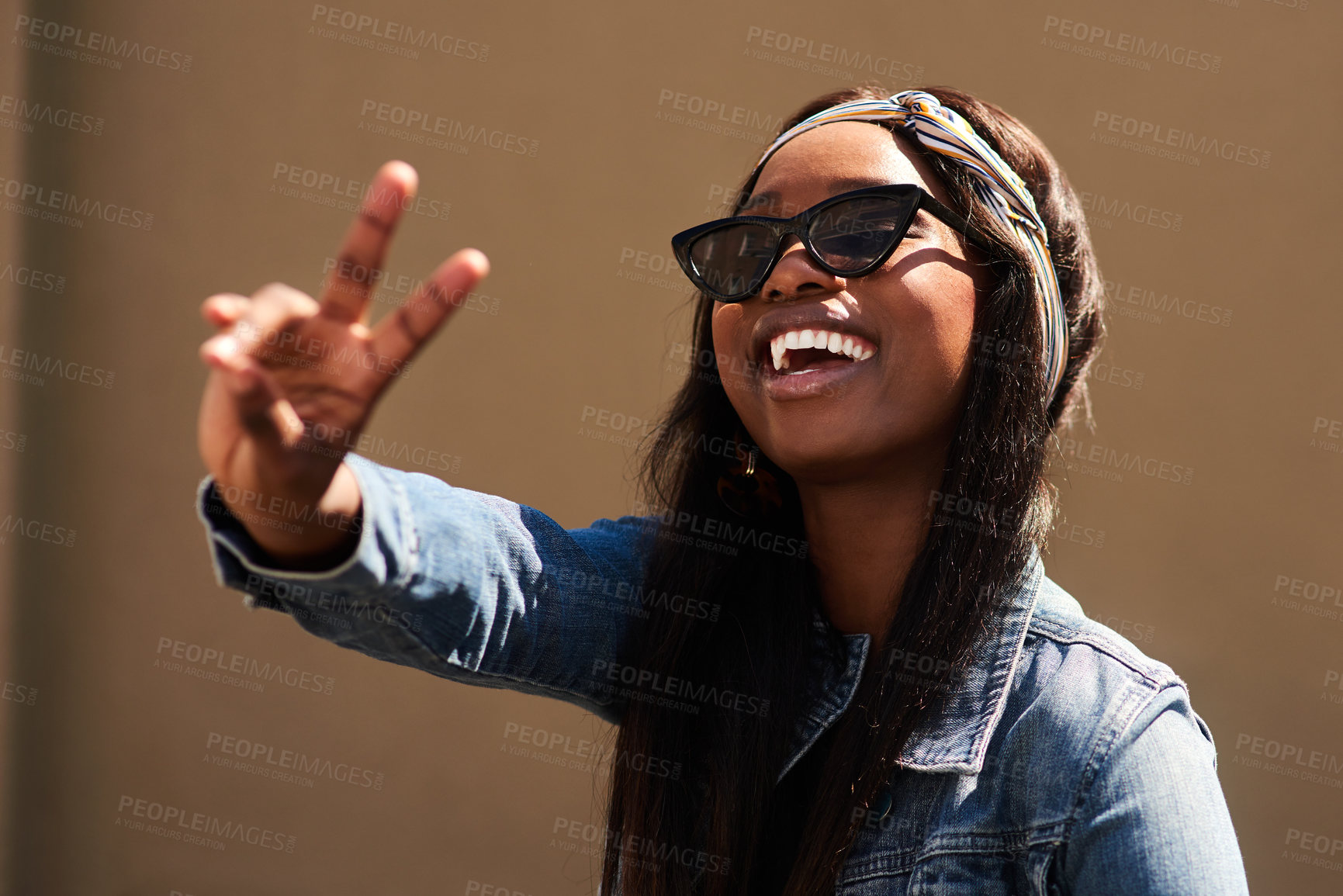 Buy stock photo Cropped portrait of an attractive young woman wearing sunglasses and making a peace sign while standing against a wall alone