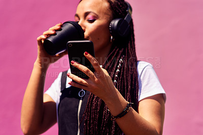 Buy stock photo Cropped shot of an attractive young woman standing against a pink wall alone and drinking coffee while using technology