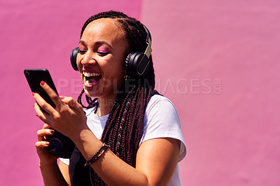 Buy stock photo Cropped shot of an attractive young woman standing against a pink wall and laughing while using technology