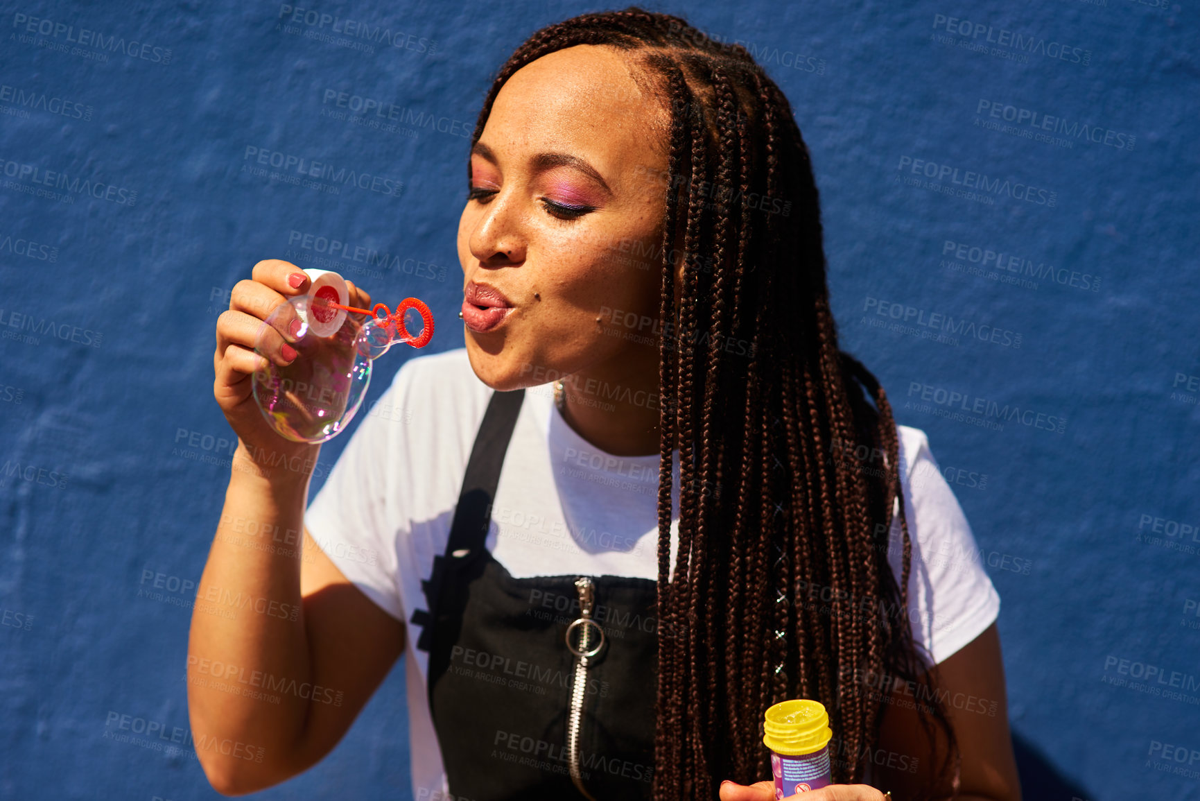 Buy stock photo Cropped shot of an attractive young woman standing against a blue wall alone and blowing bubbles while outdoors
