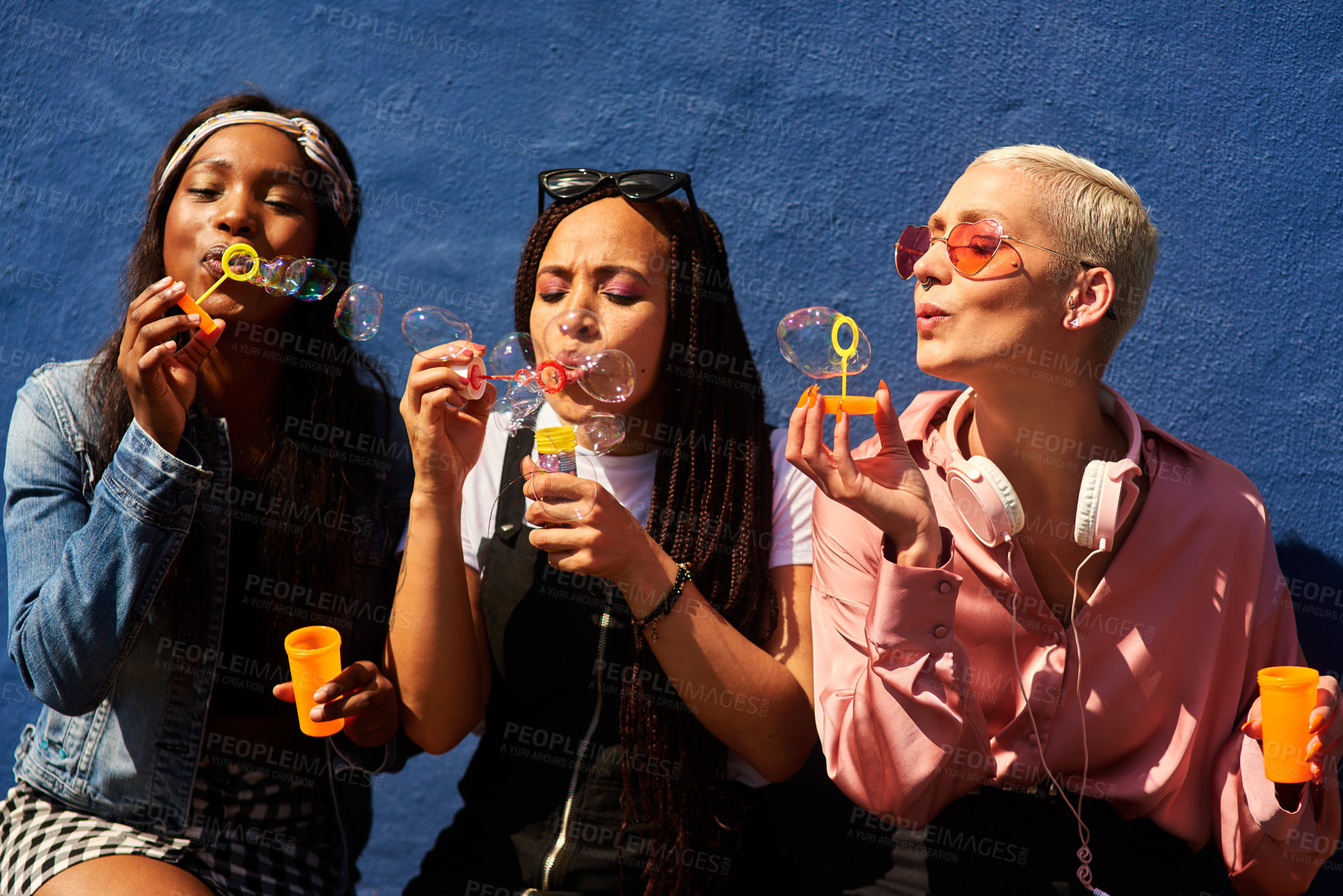 Buy stock photo Bubbles women and diverse friends on summer vacation, holiday travel or bonding activity and against a blue wall. Happy, game and ladies playing with soap or wand toy or in freedom and social break